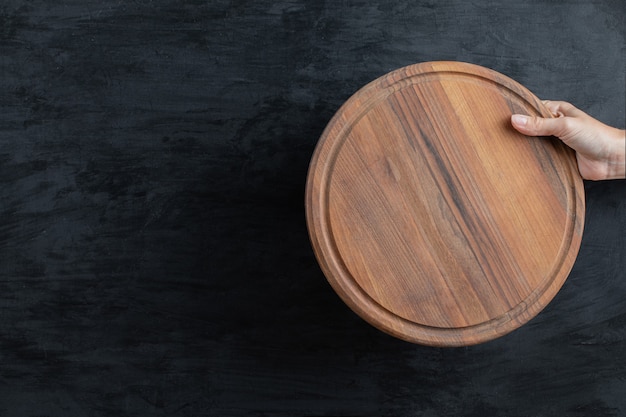 Free photo holding a round wooden platter in the hand