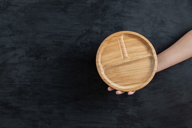 Держа в руке круглое деревянное блюдо