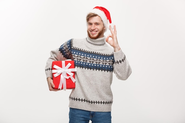휴일 개념 스웨터에 상자를 들고 확인 표시를 주는 젊은 수염 남자