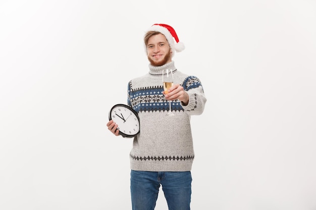 Holiday concept Young handsome beard man in sweater with white clock and champagne over white studio background