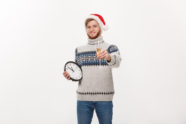 Holiday concept Young handsome beard man in sweater with white clock and champagne over white studio background