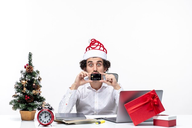 산타 클로스 모자와 은행 카드를 보여주는 놀란 비즈니스 사람과 사무실에서 휴일 축제 분위기