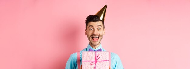 Free photo holidays and celebration concept closeup of happy guy in party hat receive birthday gift scream of j