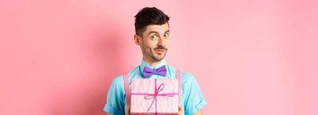 Free photo holidays and celebration concept funny guy with moustache showing cute gift box wrapped in festive p