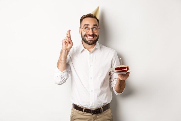 休日とお祝い。誕生日パーティーを持っている幸せな男、b-dayケーキに願い事をし、幸運のために指を交差させ、立っている