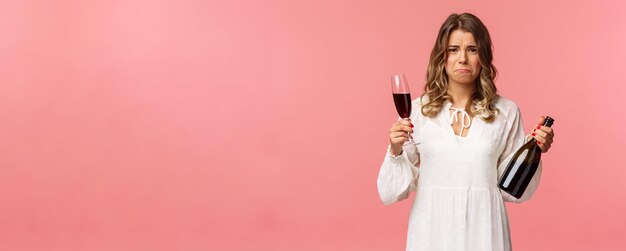 Holidays spring and party concept Portrait of upset and whining young blond woman being cheated trying to ease pain with alcohol holding glass wine and bottle grimacing want cry complaining