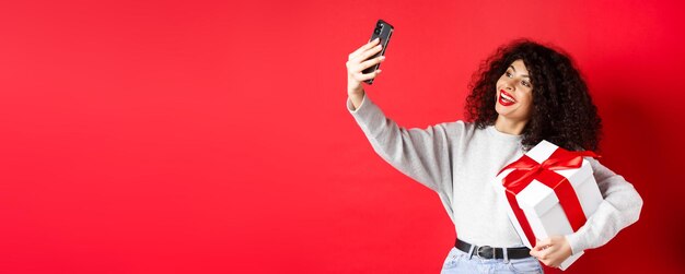 holidays and tech concept happy woman taking selfie with her gift holding present and smartphone sta