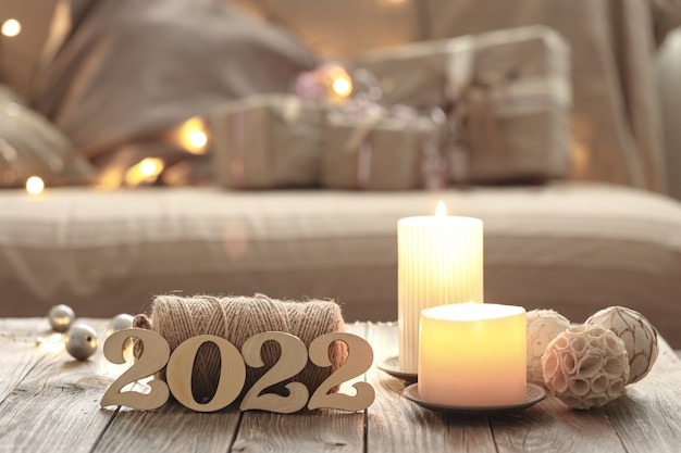 Home christmas composition with decorative wood 2022 numbers, candles, and decor details on a blurred room interior background.