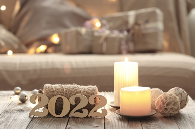 Home Christmas composition with decorative wood 2022 numbers, candles, and decor details on a blurred room interior background.