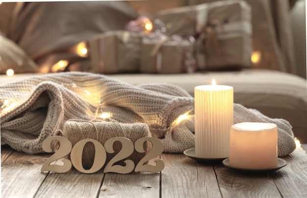 Home christmas composition with decorative wood 2022 numbers, candles, and decor details on a blurred room interior background.