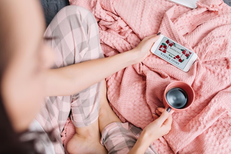 無料Photo 電話で映画を見てきれいな女性の近代的なアパートのベッドの上の家の快適さ。ピンクの毛布で国内の調和、週末、おはようを楽しんでいるコーヒーのカップを持つ女性の上からの眺め