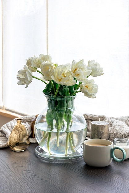 Home composition with a bouquet of tulips in a glass vase and candles