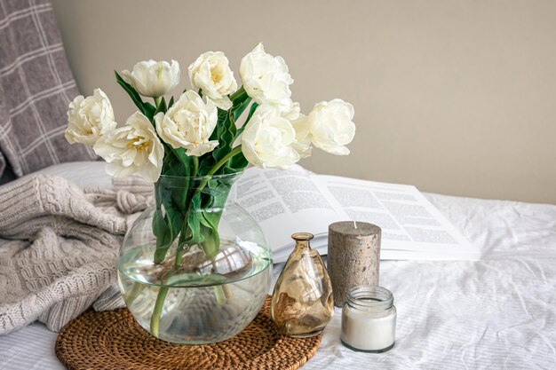 Home composition with a bouquet of tulips in a glass vase and candles