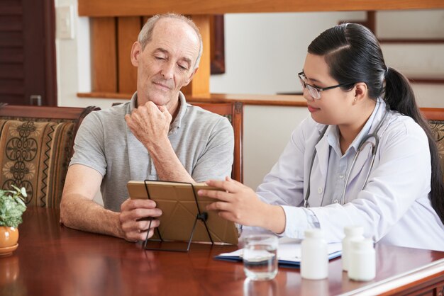 Home doctor showing test results to elderly patient on tablet PC 