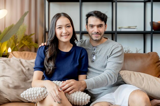 Концепция домашней изоляции счастье азиатская и кавказская любовь пара семьяхороший разговор на диване диван в гостиной жениться пара смеется улыбка вместе на диване