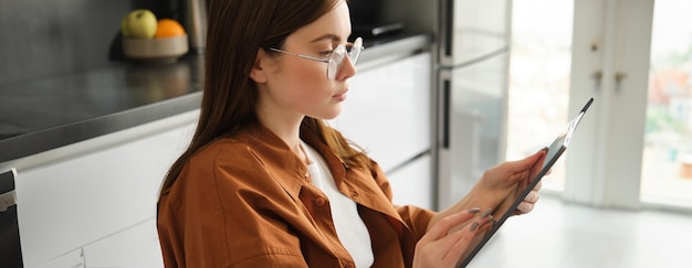 Free photo home and leisure concept portrait of beautiful young woman reading on digital tablet sitting in