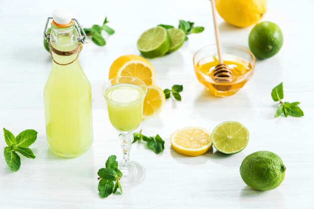 Home lime liquor in a glass and fresh lemons and limes on white