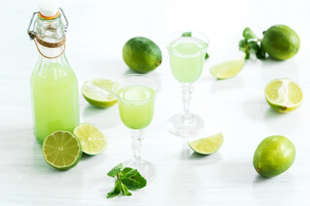 Home lime liquor in a glass and fresh lemons and limes on white