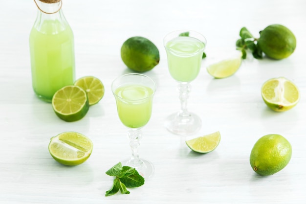 Home lime liquor in a glass and fresh lemons and limes on white