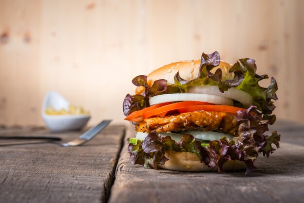 Домашний куриный бургер с картофелем фри, салатом, томатом и луком на деревянной доске.