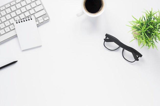 Home office workspace mockup with spiral notepad; keyboard; coffee; eyeglasses and plant