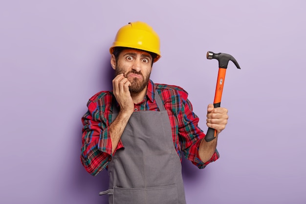 Home renovation concept. Indignant builder holds hammer, does repairing