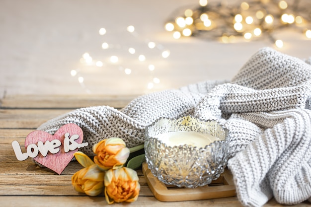 Home romantic still life with candle, decor, fresh flowers and knitted element on blurred background with bokeh.