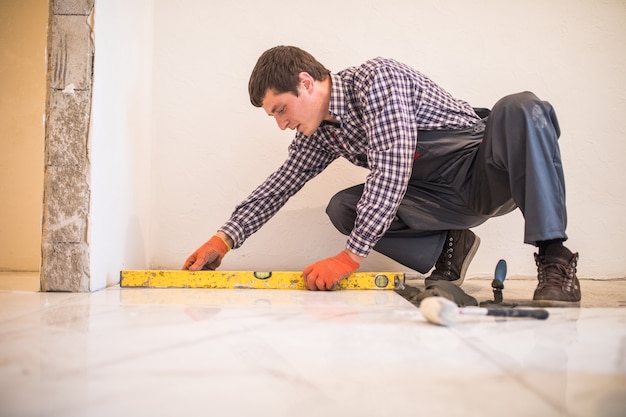 Home tile improvement - handyman with level laying down tile floor