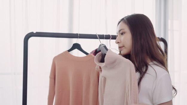 Home wardrobe or clothing shop changing room. Asian young woman choosing her fashion outfit clothes 