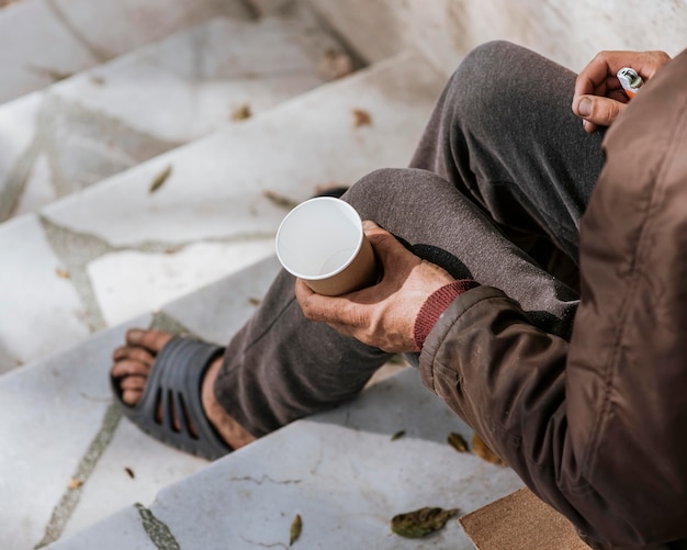 Homeless man holding empty cup on stairs