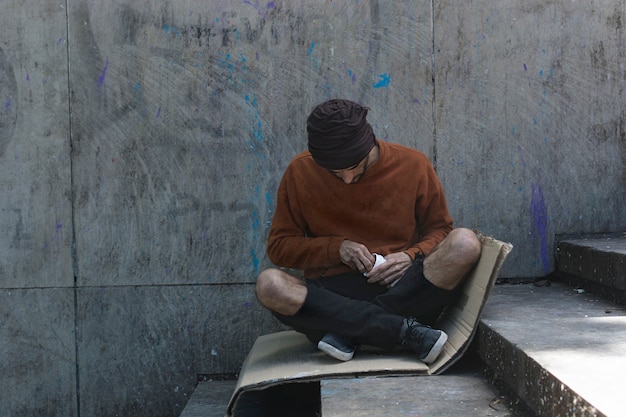 Бездомный человек сидит на картоне на улице