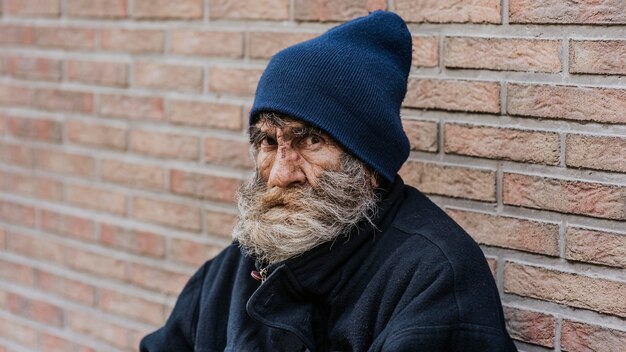 Homeless man with beard in front of wall
