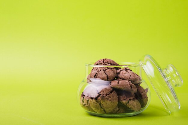 Homemade baked chocolate cookies in glass jar on green background