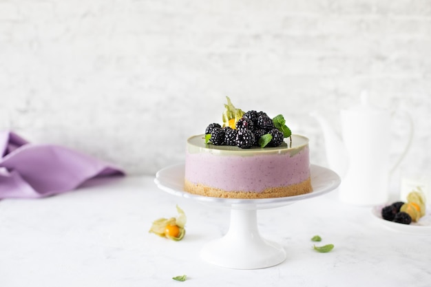 Homemade blackberry cheesecake and matcha tea on a cake stand on a white background Berry dessert Copy space