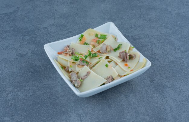 Homemade boiled dough with dried meat parts on white plate.