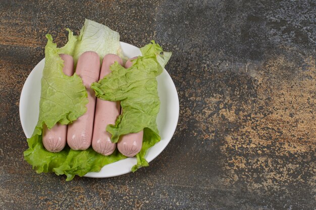 Homemade boiled sausages and lettuce on white plate.