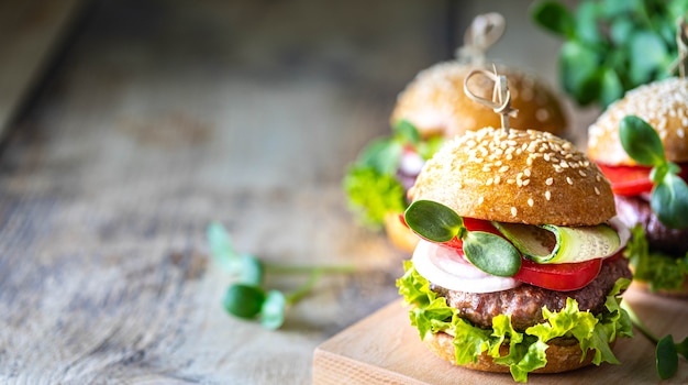 Homemade burgers with cutlet, fresh lettuce, tomatoes, onions on a wooden table. copy space