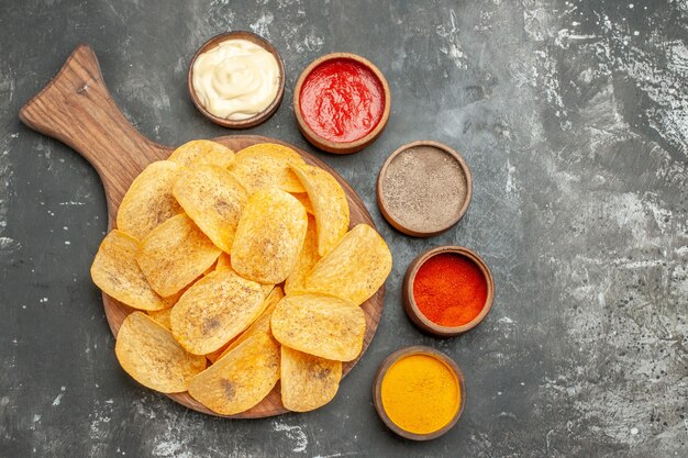 Homemade chips spices and mayonnaise with ketchup on wooden cutting board on gray table