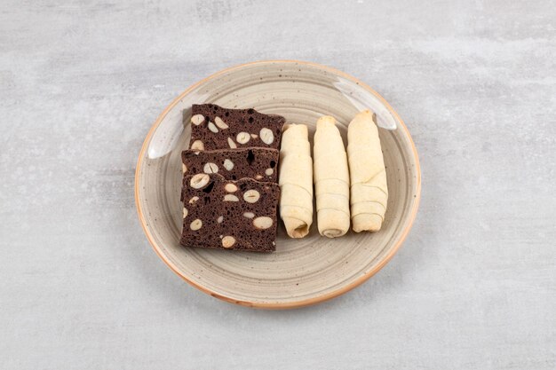 Homemade chocolate brownies and roll cookie on a dish, on the marble table. 