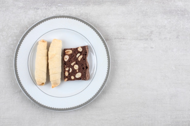 Homemade chocolate brownies and roll cookie on a plate, on the marble table. 