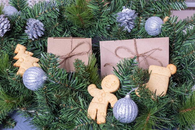 Домашнее рождественское печенье, имбирные пряники и подарки в коробках для рукоделия на столе с еловыми ветками и рождественскими серебряными шарами и шишками. рождественский фон.