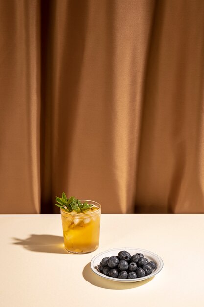 茶色のカーテンの近くの白いテーブルの上の皿にブルーベリーと自家製カクテルドリンクグラス