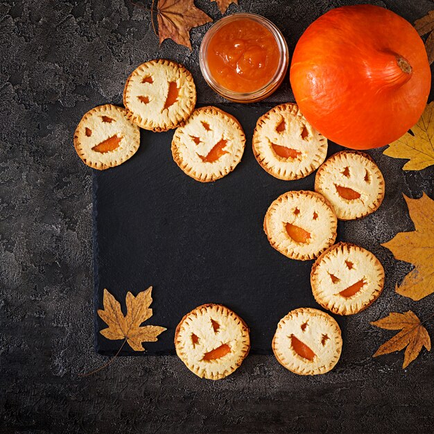 Homemade  cookies in the form as Halloween  jack-o-lantern pumpkins  on the dark table. Top view.