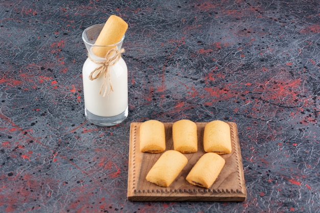 Biscotti fatti in casa su tavola di legno e una bottiglia di latte su rustico.