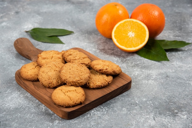 Homemade cookies on wooden board and organic oranges .