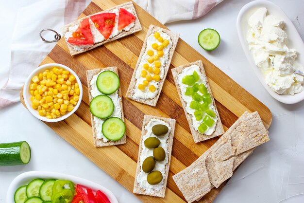 Homemade Crispbread toast with Cottage Cheese and green olives, slices of cabbage, tomatoes, corn, green pepper on cutting board. Healthy food concept, Top view. Flat Lay