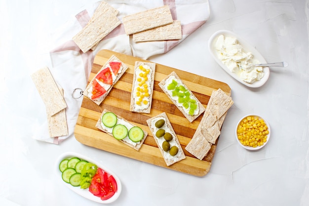 Homemade Crispbread toast with Cottage Cheese and green olives, slices of cabbage, tomatoes, corn, green pepper on cutting board. Healthy food concept, Top view. Flat Lay