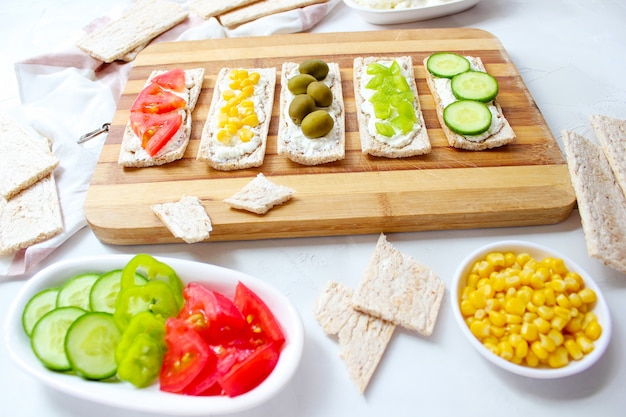 Free photo homemade crispbread toast with cottage cheese and green olives, slices of cabbage, tomatoes, corn, green pepper on cutting board. healthy food concept, top view. flat lay