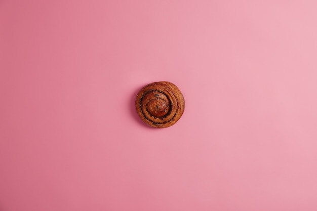 Homemade delicious appetizing cinnamon bun with caramelized sugar and jam filling isolated on pink background. Ready to eat sweet tasty swirl roll. Bakery, nutrition, unhealthy food concept.