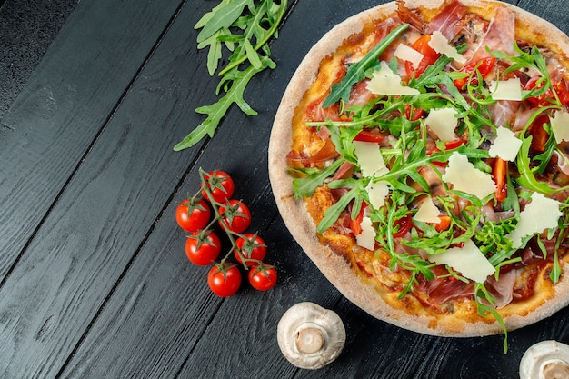 Homemade fresh pizza with arugula, parmesan and cherry tomatoes on a black wooden with copy space.